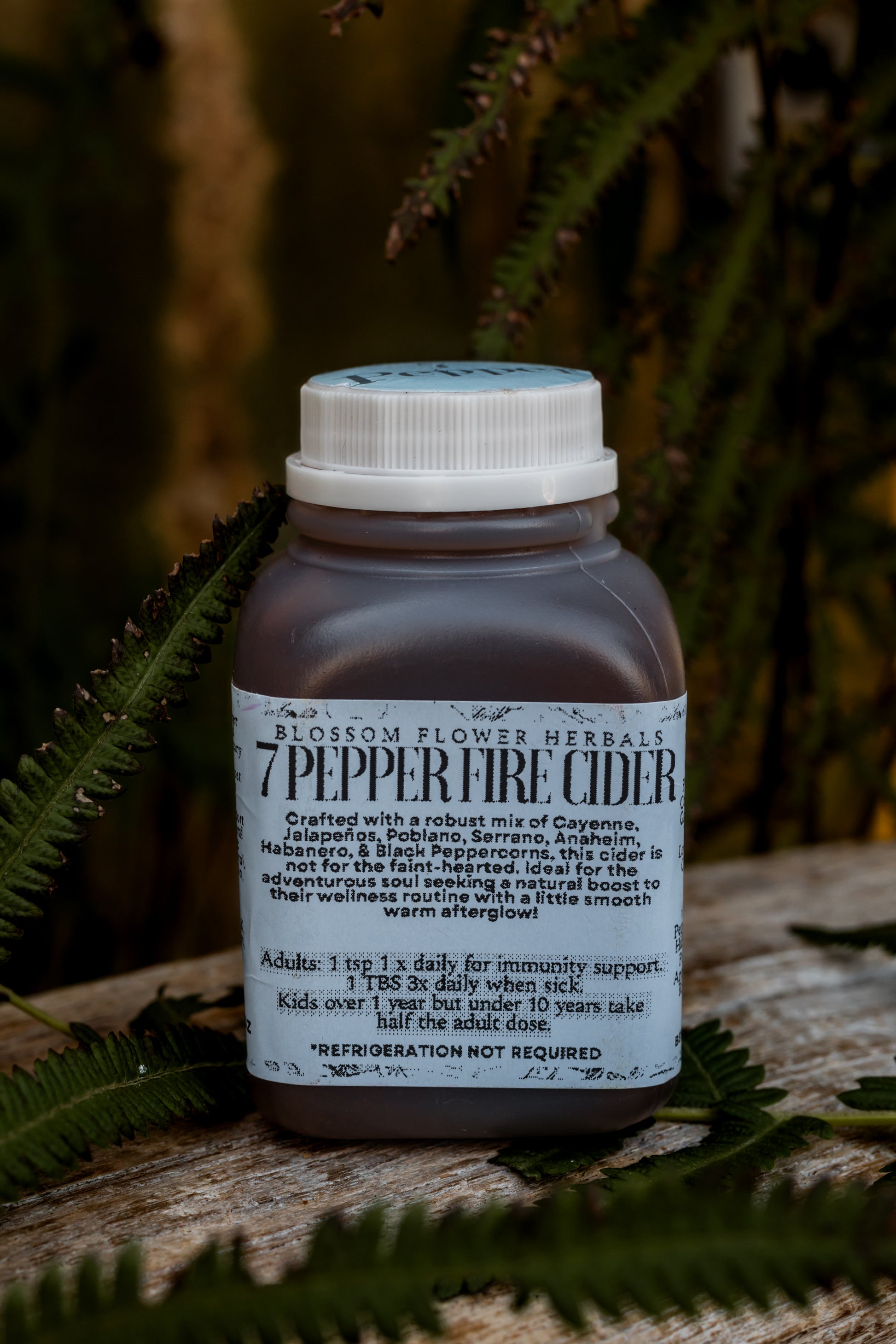 A vibrant bottle of 7 Pepper Fire Cider, showcasing a golden orange hue with flecks of rich red and earthy spices, representing its bold, zesty, and fiery flavor profile.